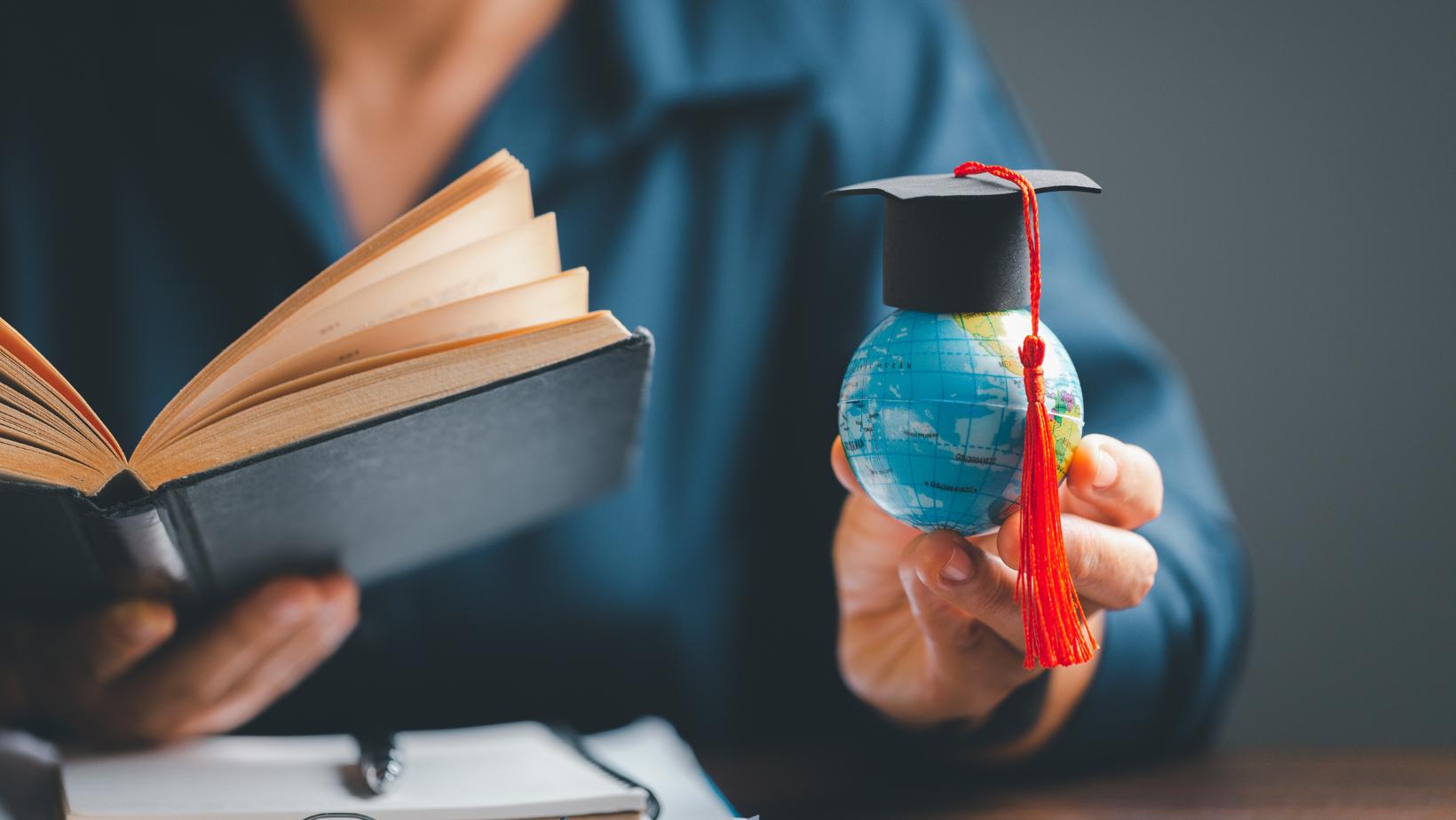 A lady is holding a globe with a graduation cap on it.