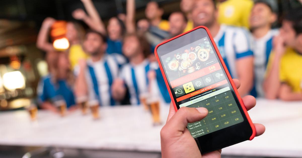 Close-up image of a sports app displayed on a phone with enthusiastic football fans in the background, capturing the excitement of the game.